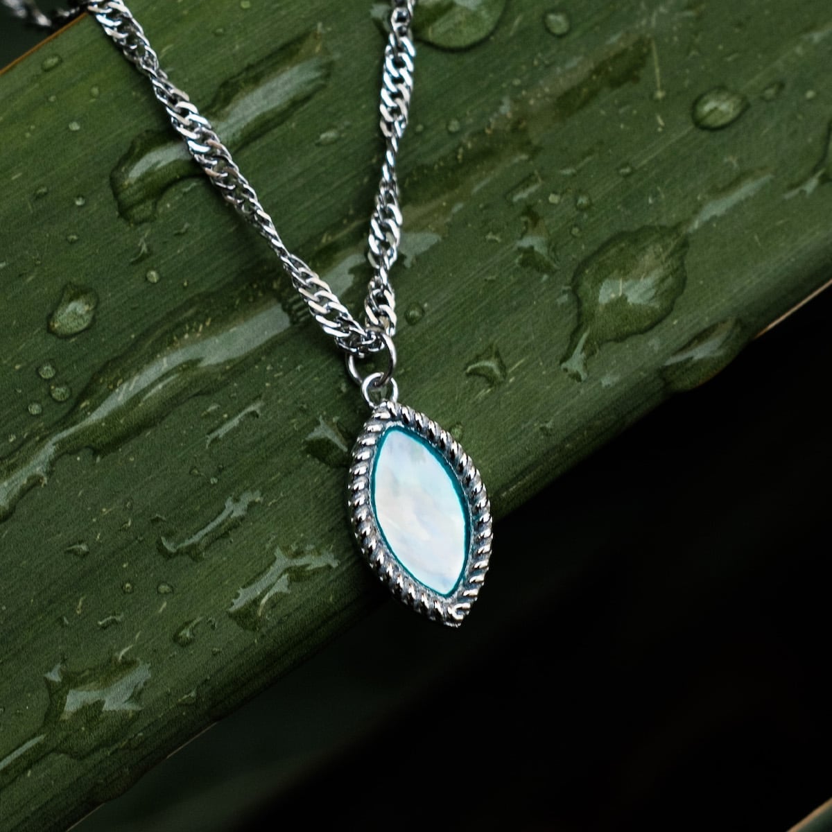 "Visual Necklace", an elegant necklace with nacre and silver detailing, against a dewy green backdrop.