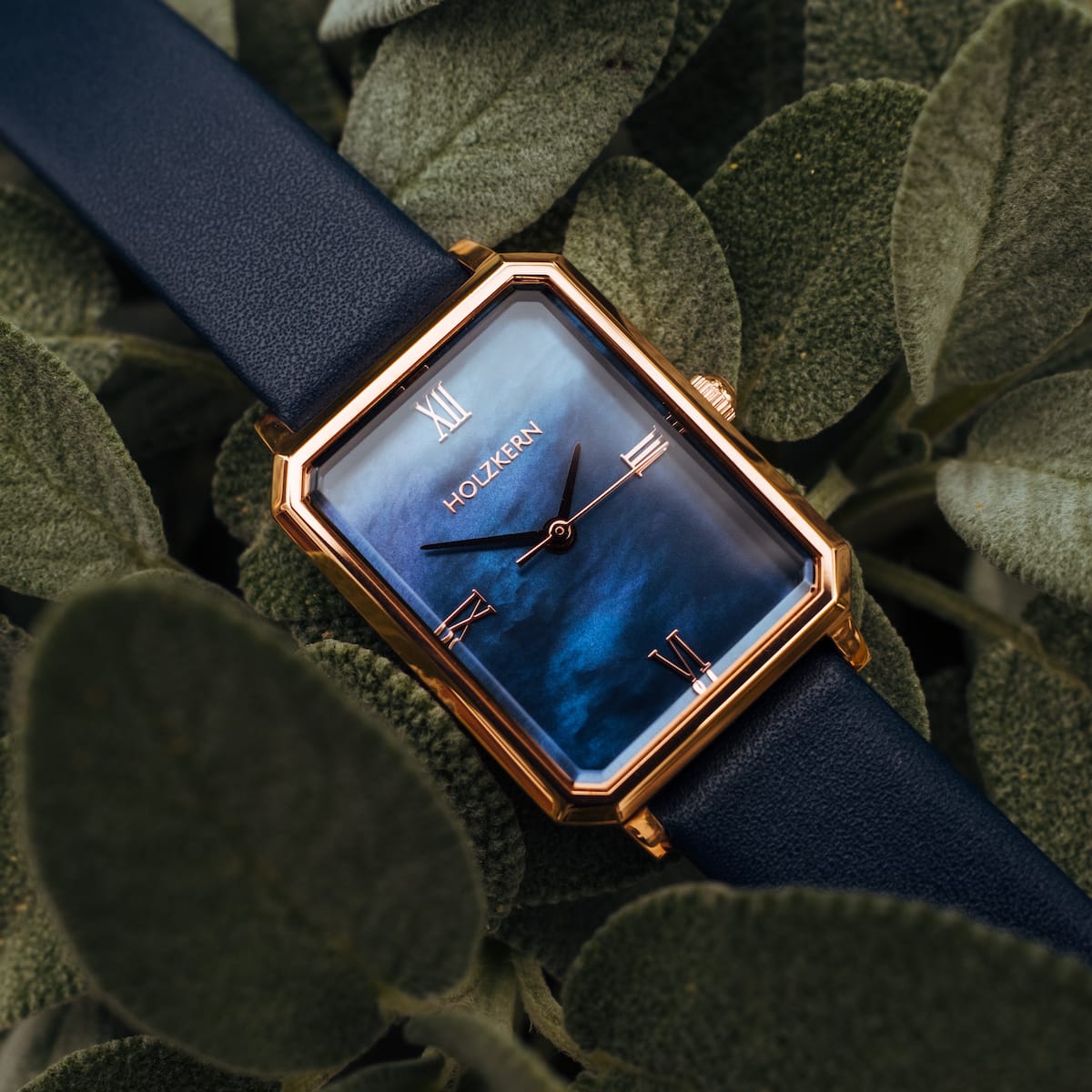 "Sapientia" watch featuring a rose gold frame and nacre dial set against lush green foliage.