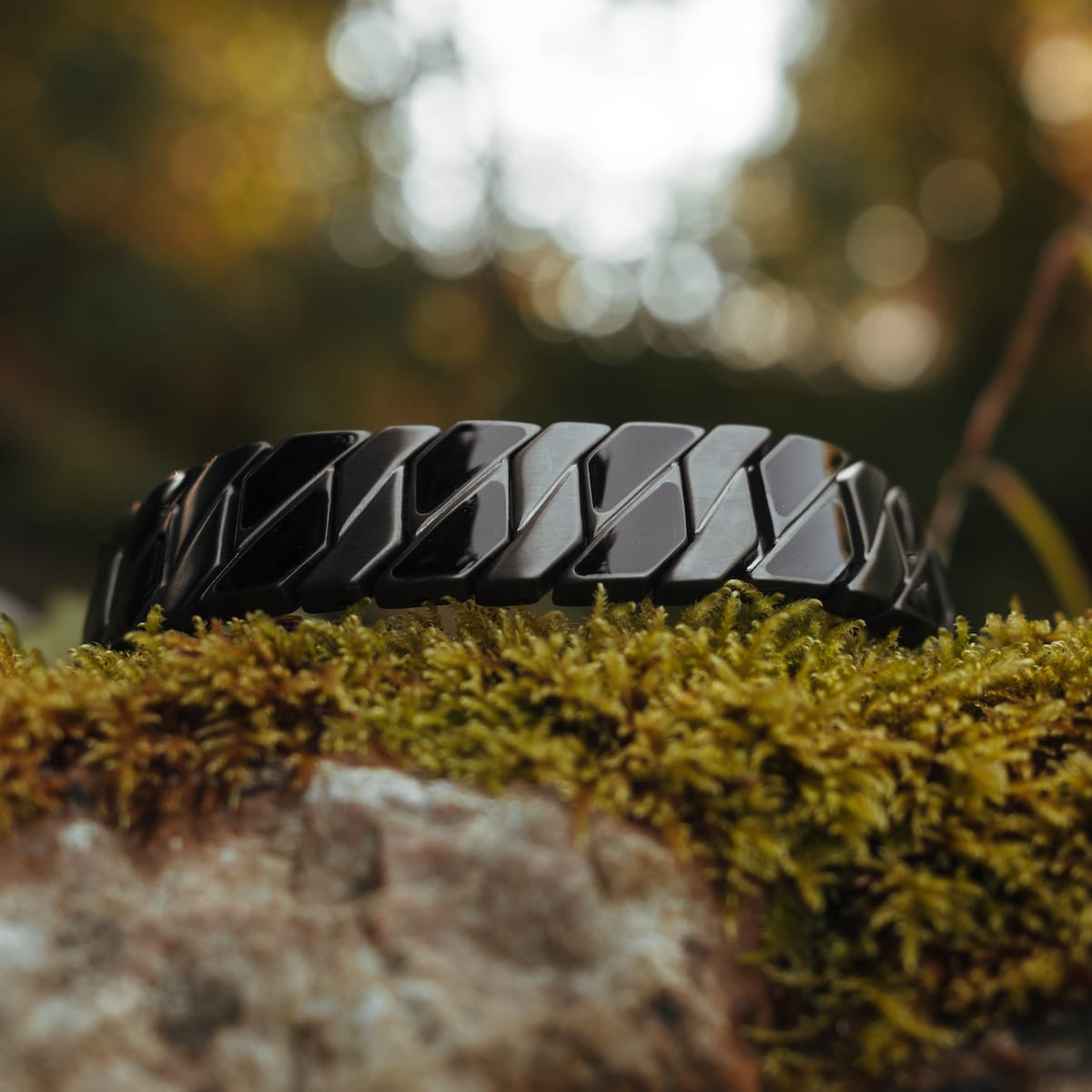 "Baritone" bracelet, sleek design in maple and dark grey, displayed on natural mossy background.