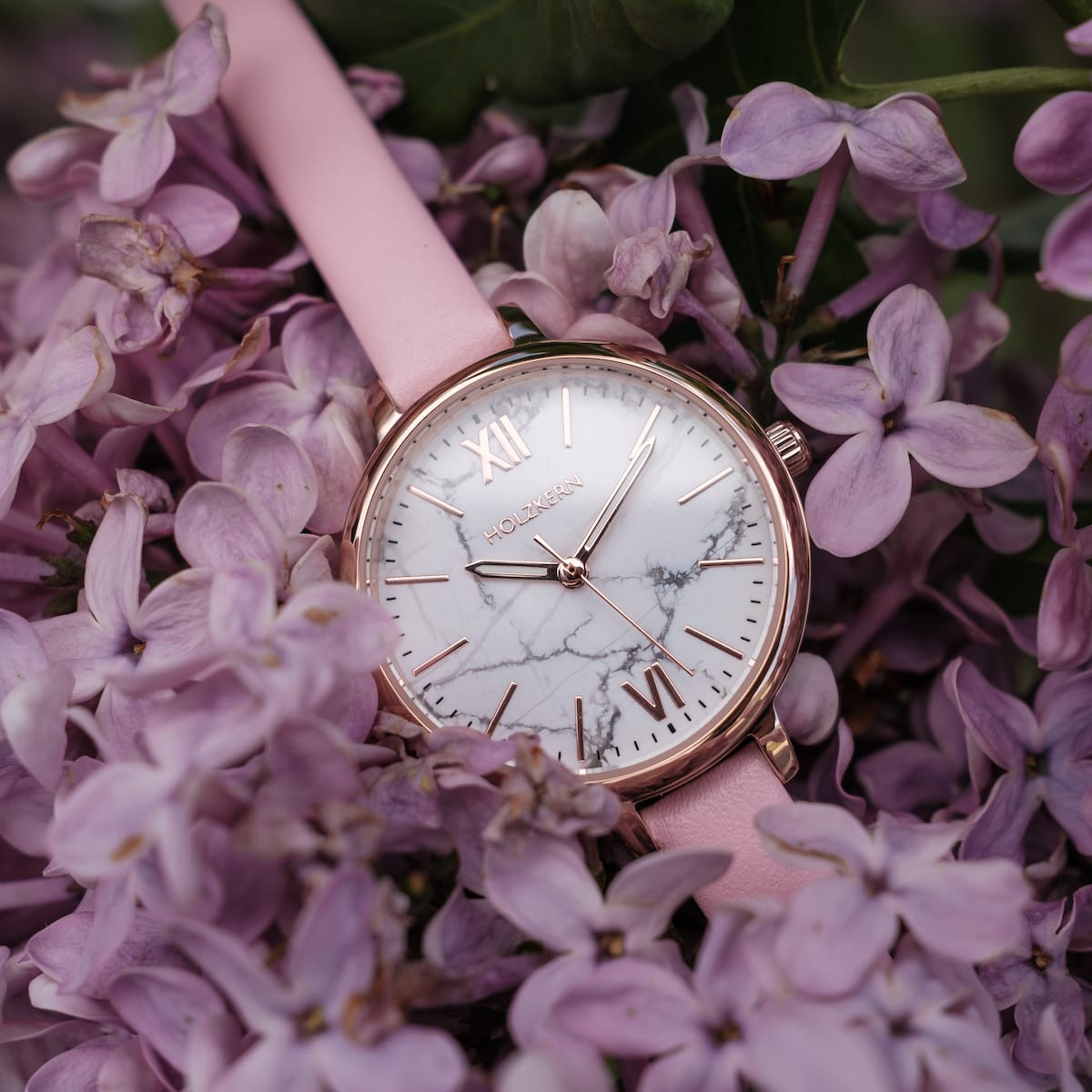 "Alva" watch featuring a marble dial and rose gold accents, set against delicate blooms.