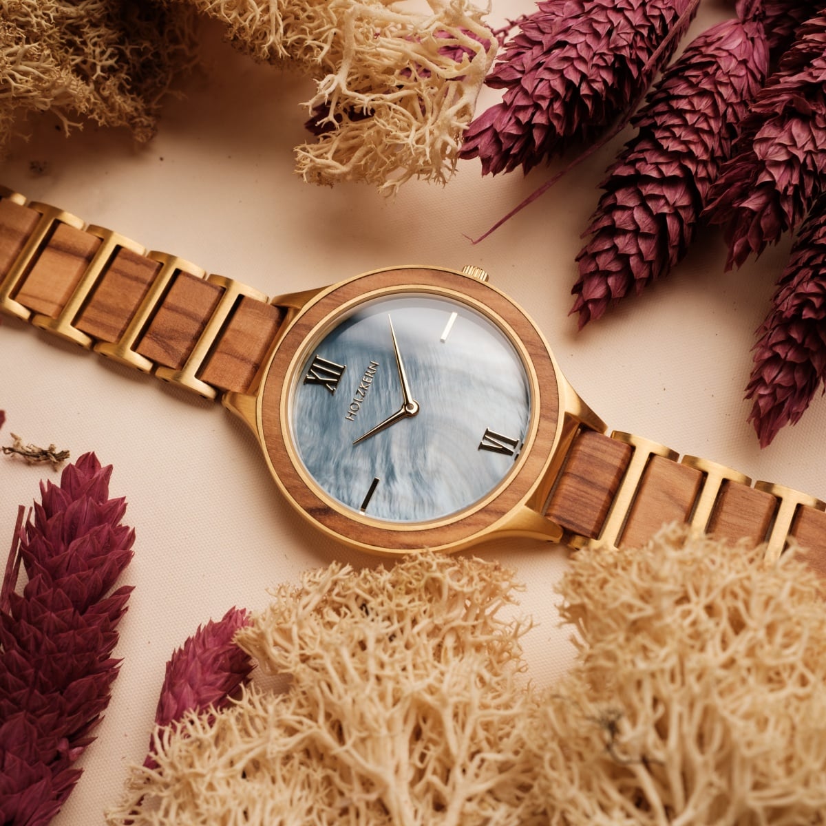 "Capri" watch with a natural wood finish and elegant nacre dial, surrounded by dried foliage.