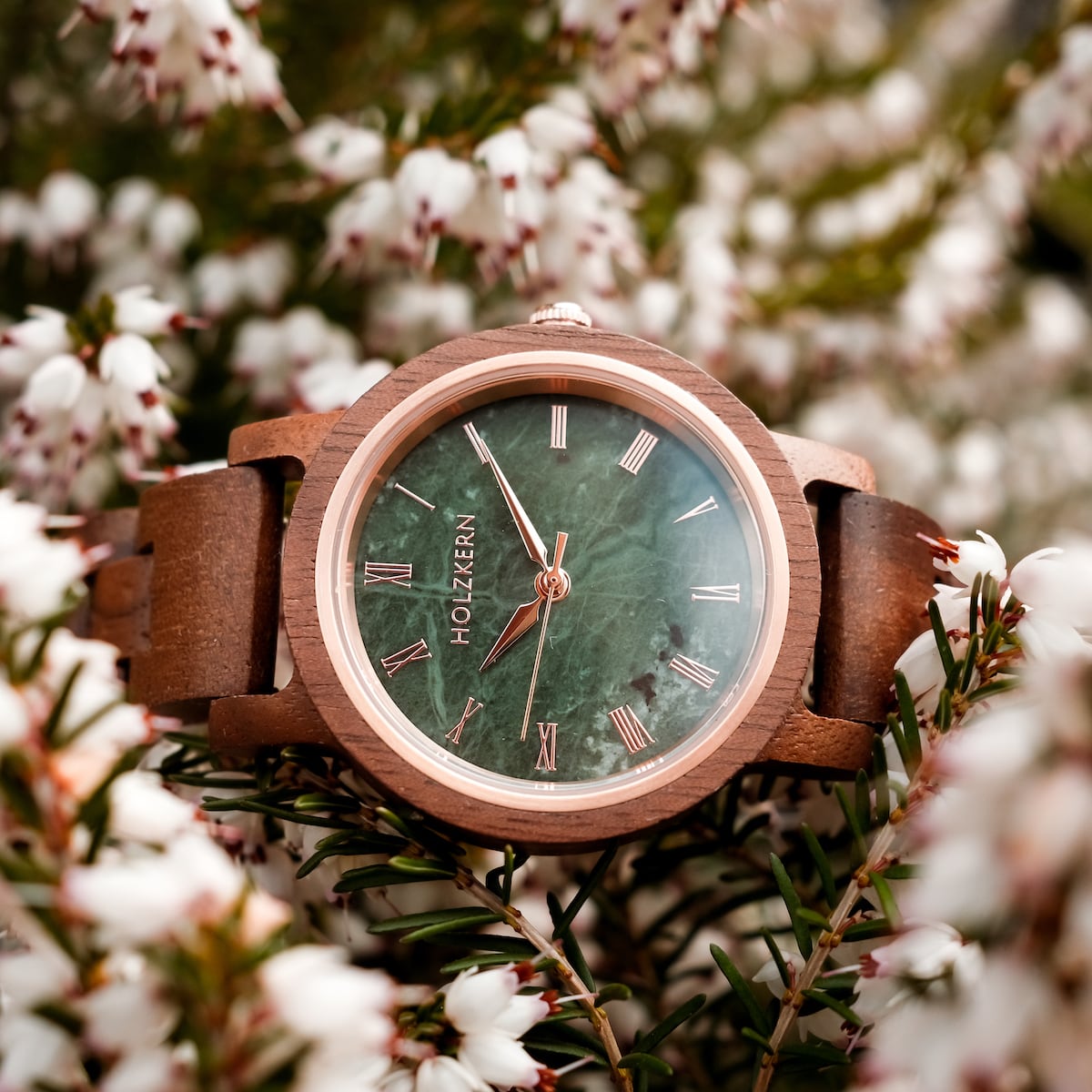 "Nymph" watch with Walnut body and marble dial, surrounded by blooming flowers.