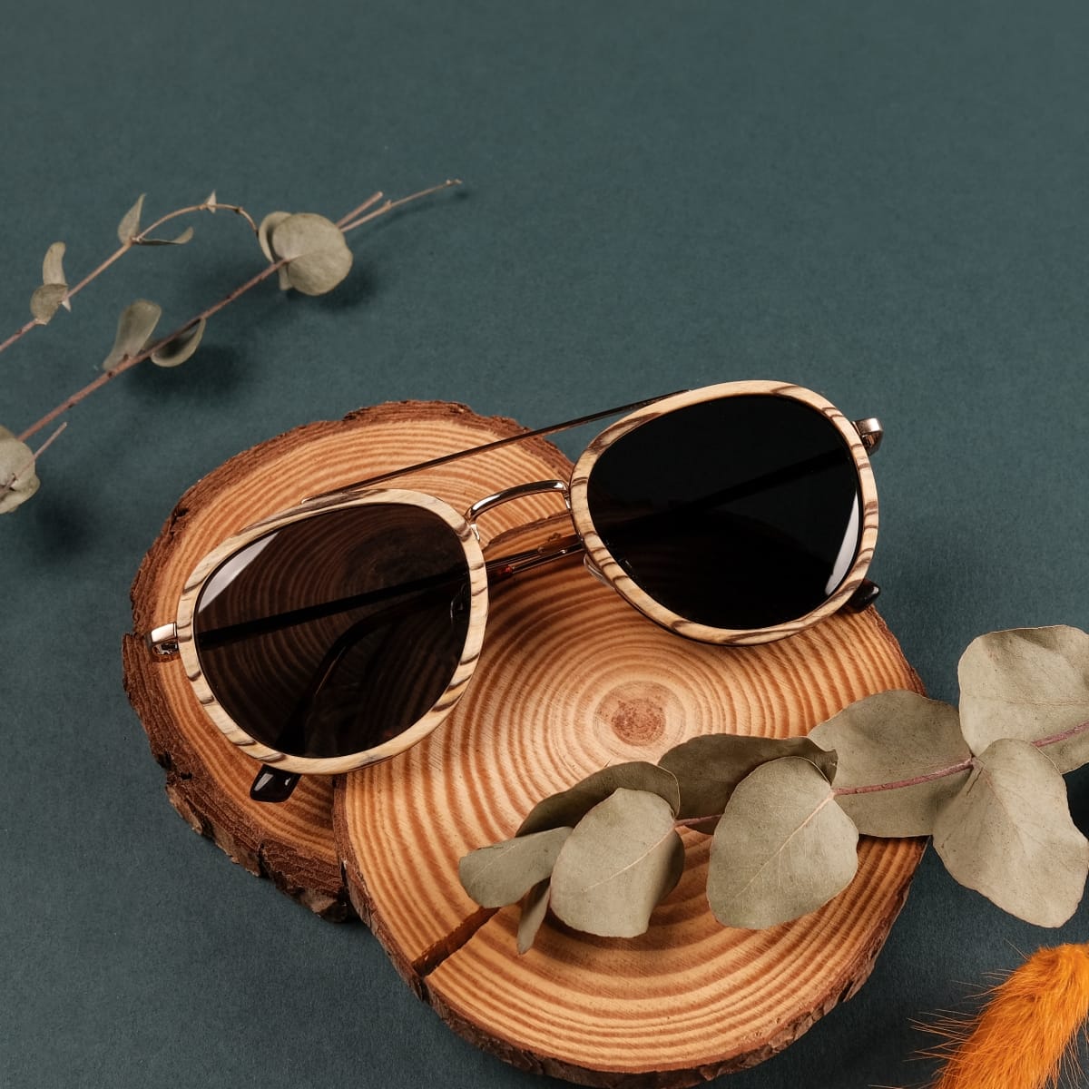 "The Risky" sunglasses with zebrawood frame and matte gold accents on a rustic background.
