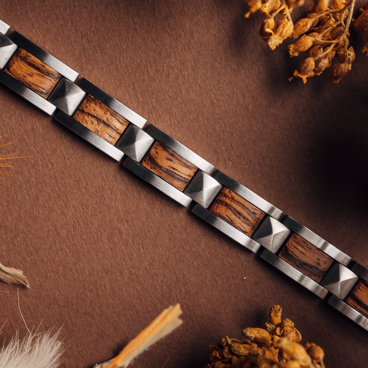 "Rhapsody" bracelet features a sleek design with zebrawood and silver tones, set against a warm, textured backdrop.