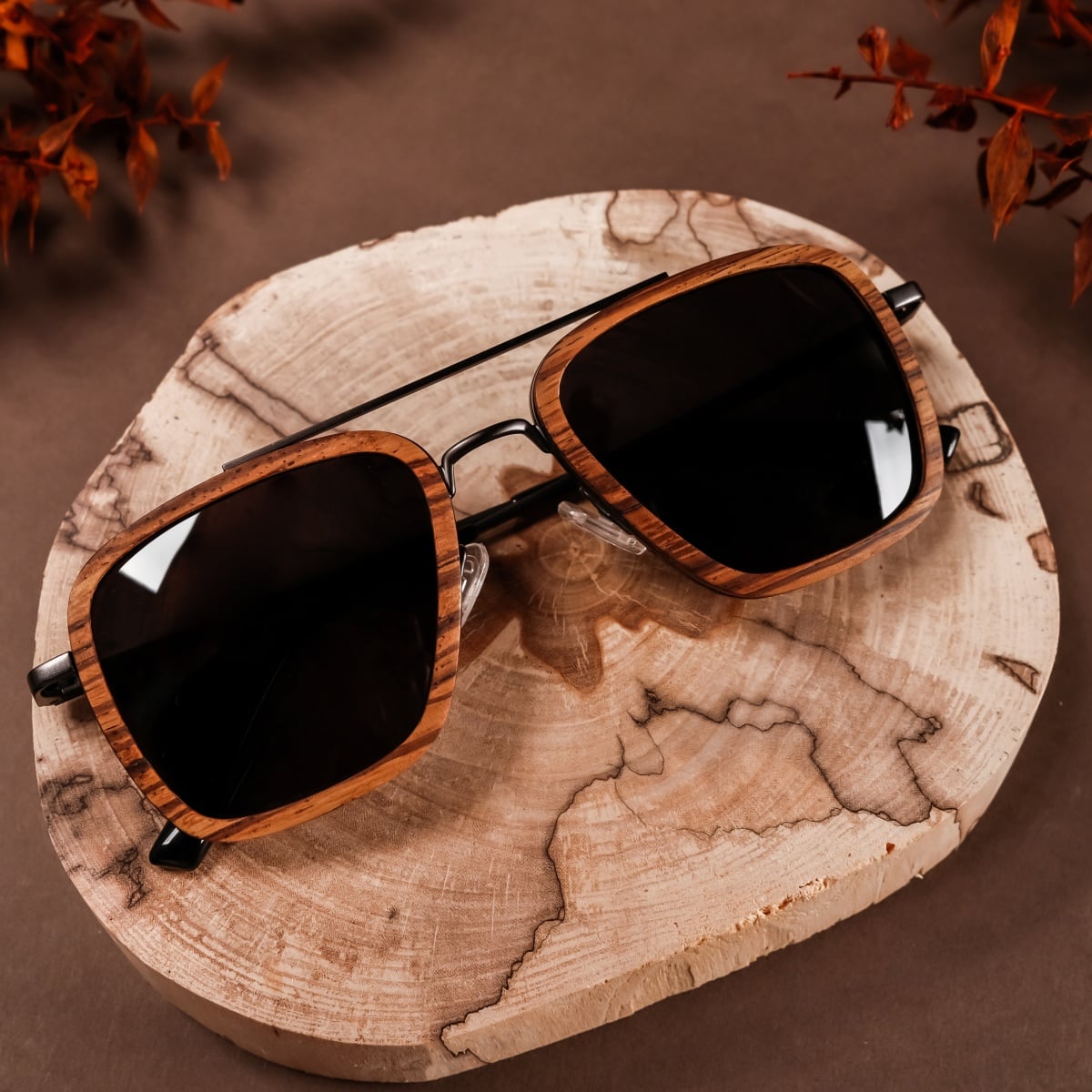 "The Logician" sunglasses, featuring a zebrawood and dark grey style on a rustic background.