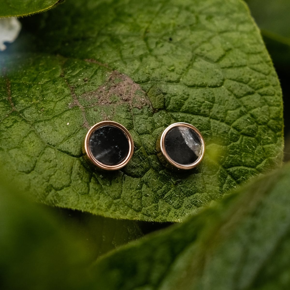 "Pigment Earrings" earrings featuring a marble and rose gold design against a leafy background.