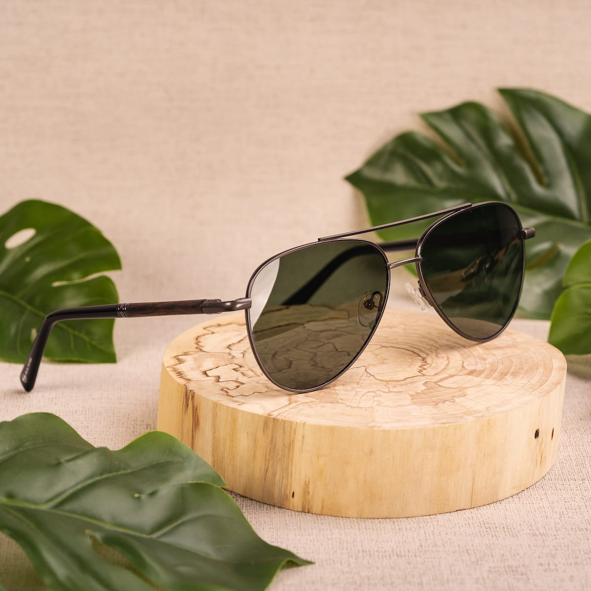 "The Badass II" sunglasses in Leadwood and Antique Silver, featuring a sleek aviator style on a wooden display.