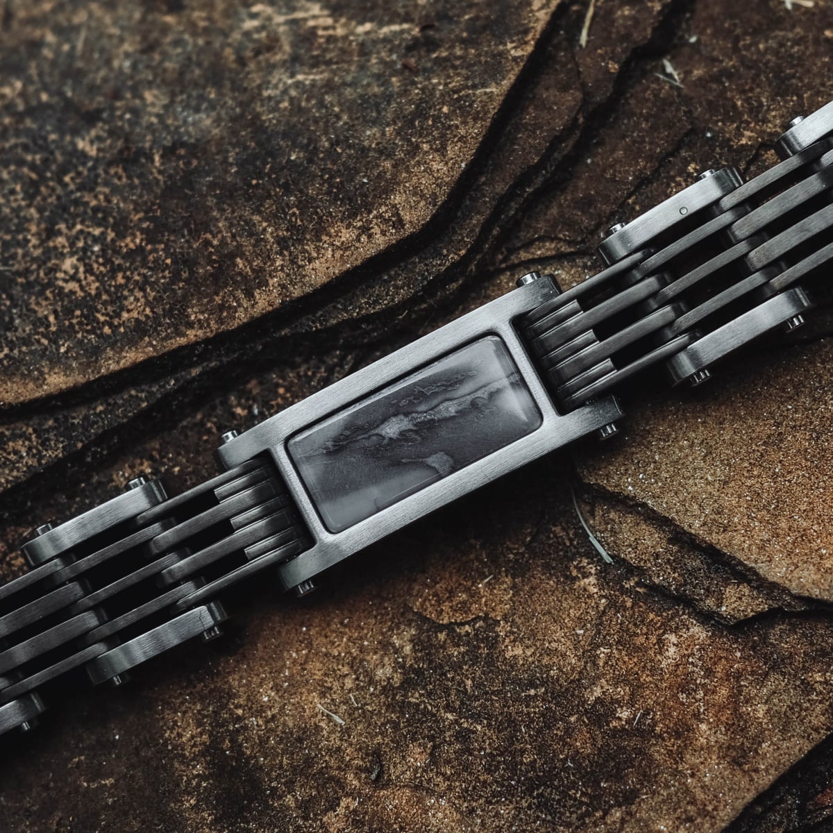 "Adagio" bracelet with a marble-gray aesthetic, featuring sleek metallic links on a stone background.