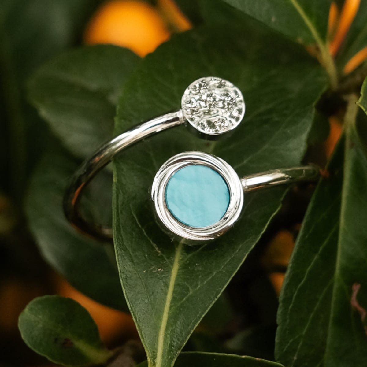 "Zendala Ring", a stylish ring with nacre and silver detailing, set against a natural leafy background.