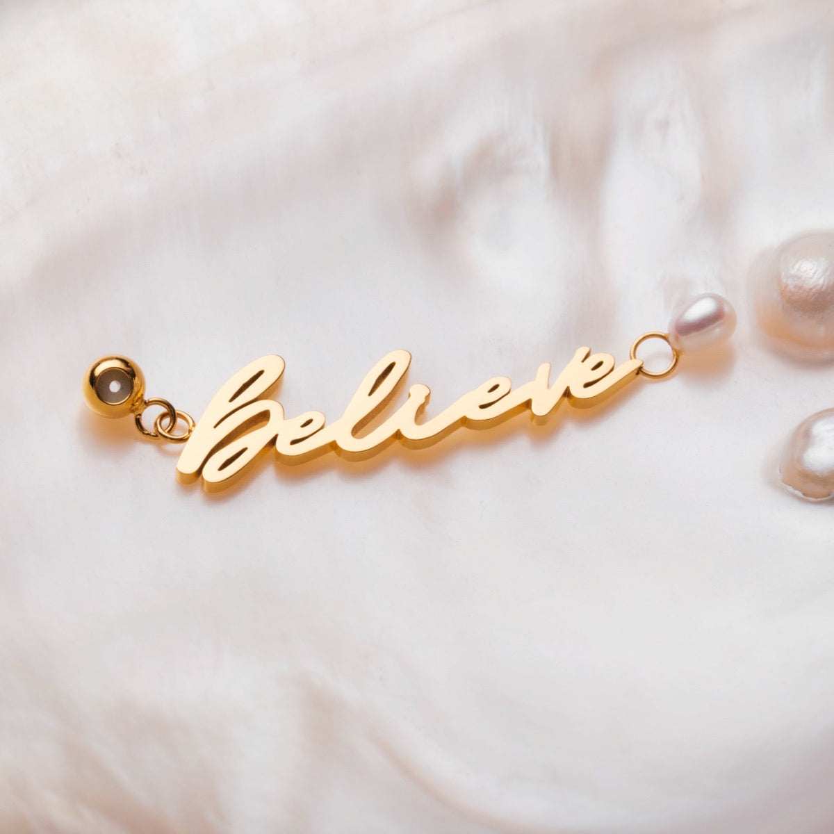 "Believe-Charm" gold charm with pearls, featuring a cursive "Believe" design on a soft background.