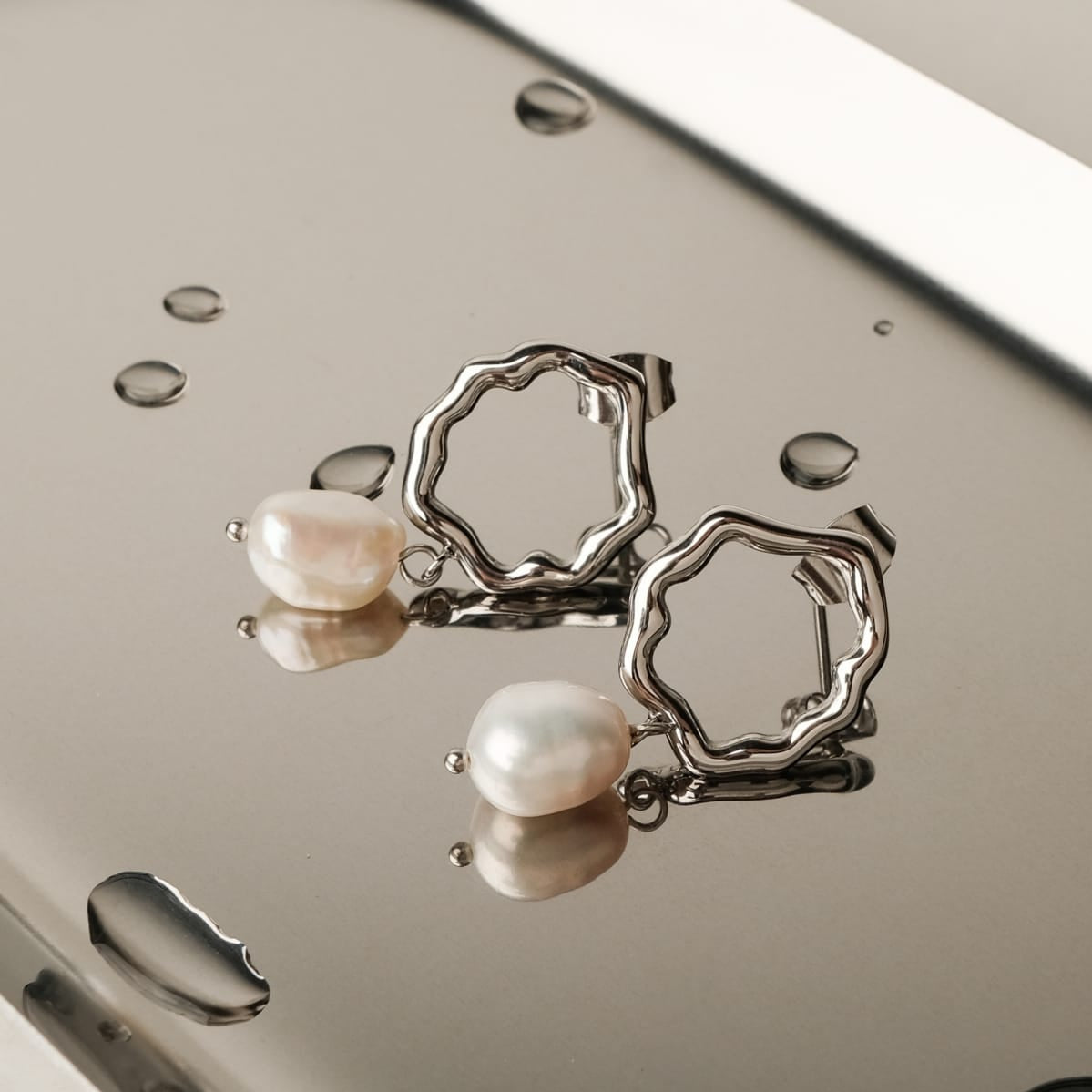Oceanfoam Earrings featuring a wavy silver design with elegant pearl detailing on a reflective surface.