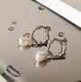 Oceanfoam Earrings featuring a wavy silver design with elegant pearl detailing on a reflective surface.
