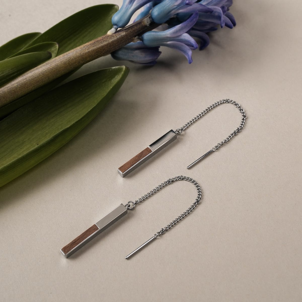 "Campania Earrings", elegant earrings with walnut and silver accents, displayed alongside a flower.