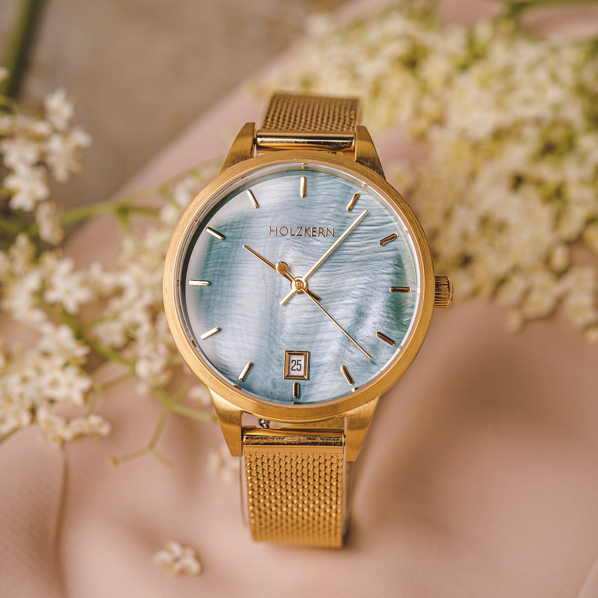 "Talamanca", elegant watch featuring a nacre dial and gold accents, set against a floral background.