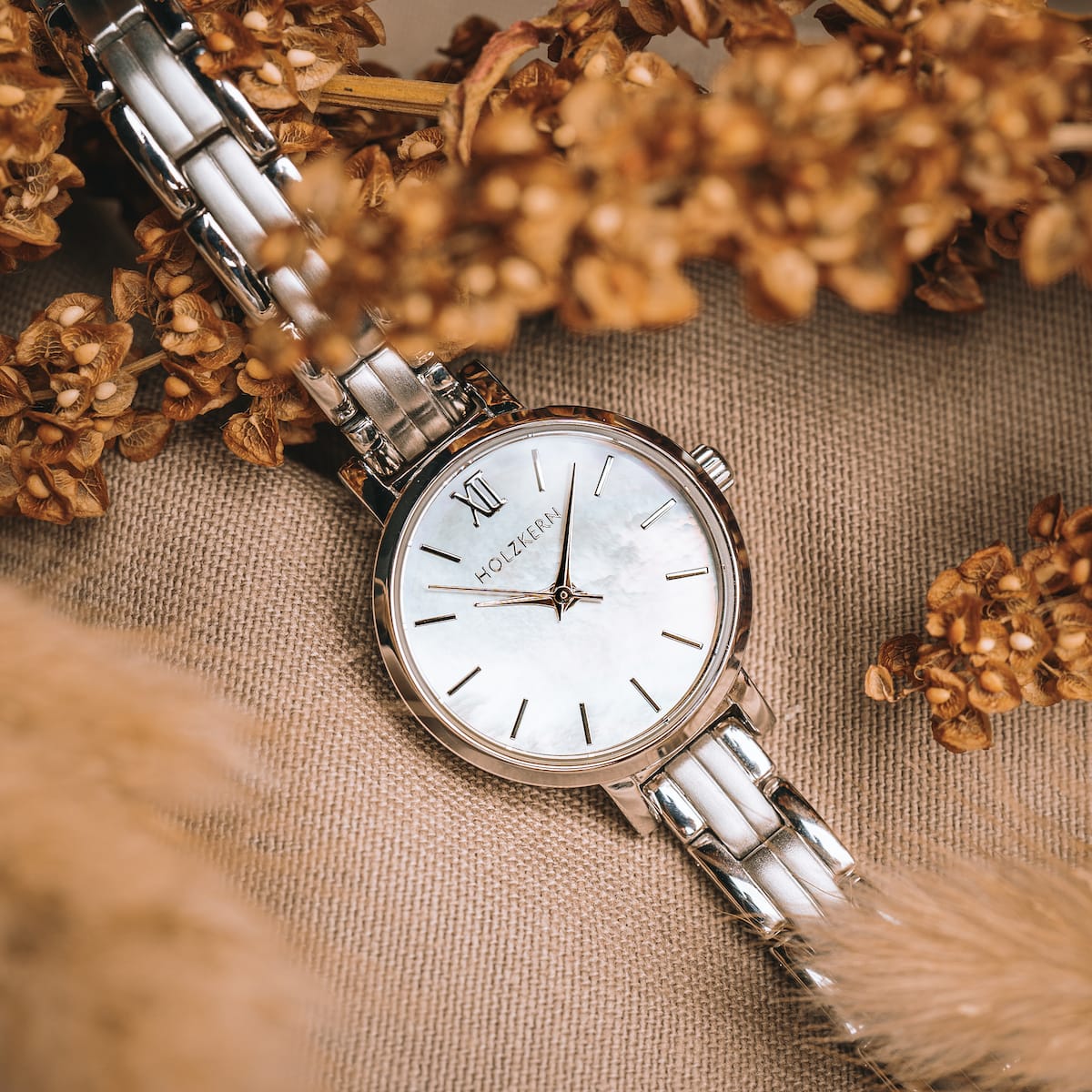 "Skadi" watch featuring a nacre dial and silver bracelet, styled elegantly amidst dried flowers.