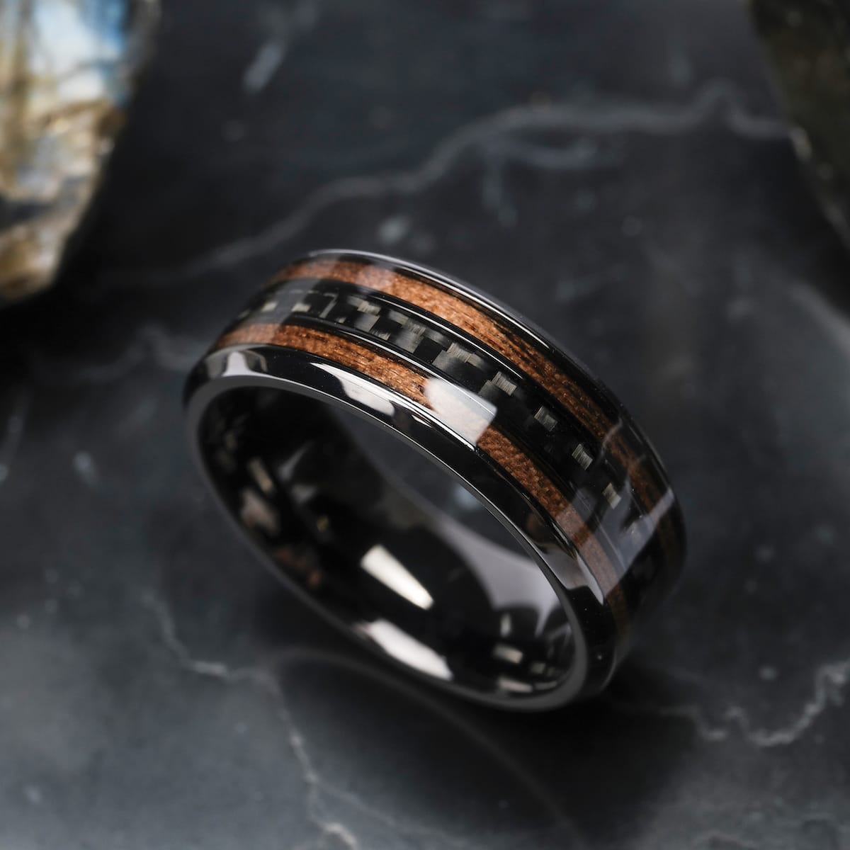 "Cartesian Ring", a stylish ring featuring a blend of walnut and carbon, set on a dark marble surface.