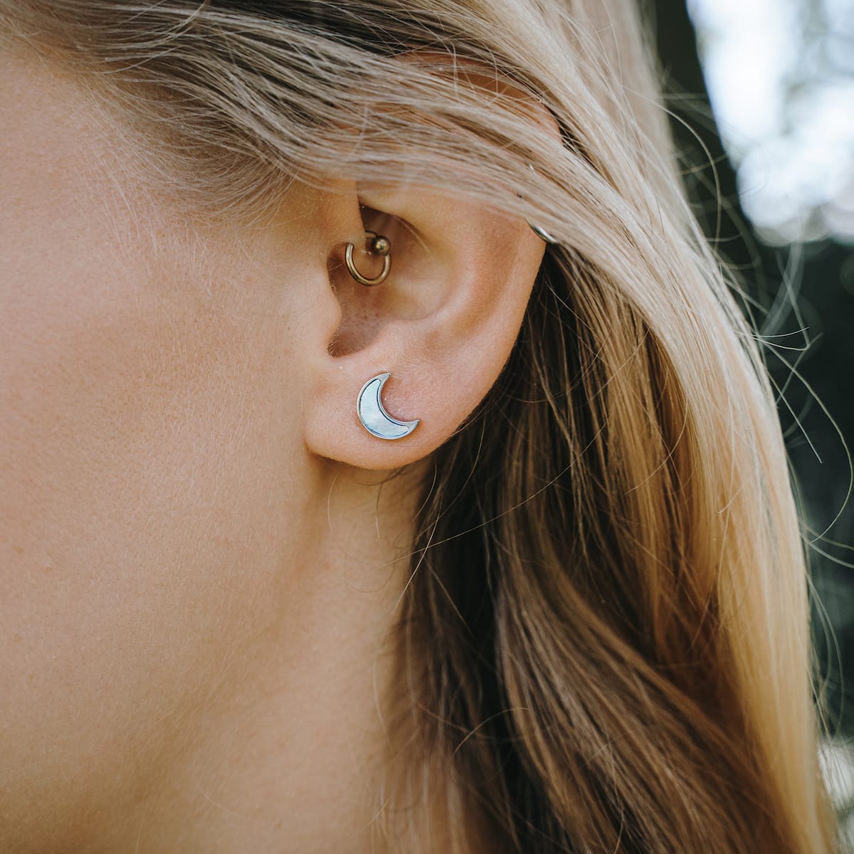 "Hue Earrings" earrings, delicate crescent shapes with blue nacre and silver accents, styled elegantly on an ear.