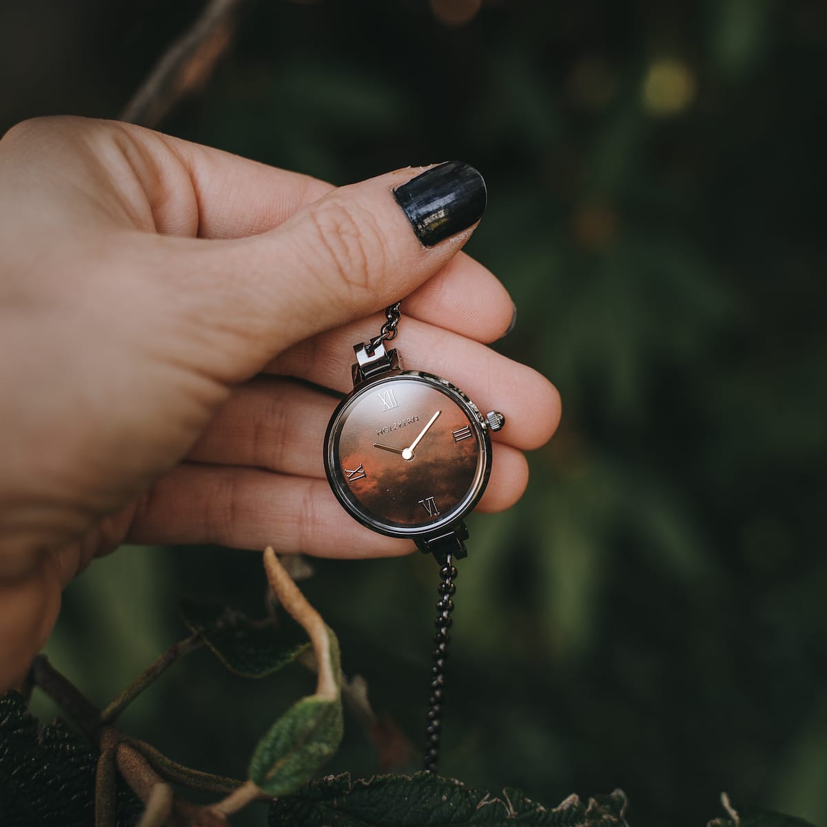 "Élisa" watch with nacre and dark gray finish, hero in hand against a natural backdrop.