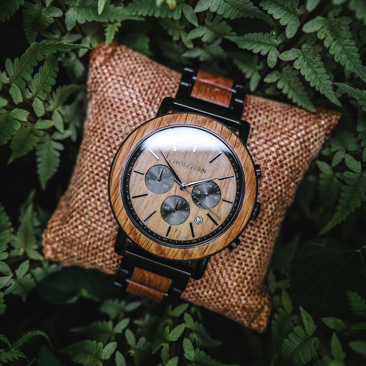 "Whakaari" watch with oak finish, featuring a classic chronograph design nestled on a cushion among fars.