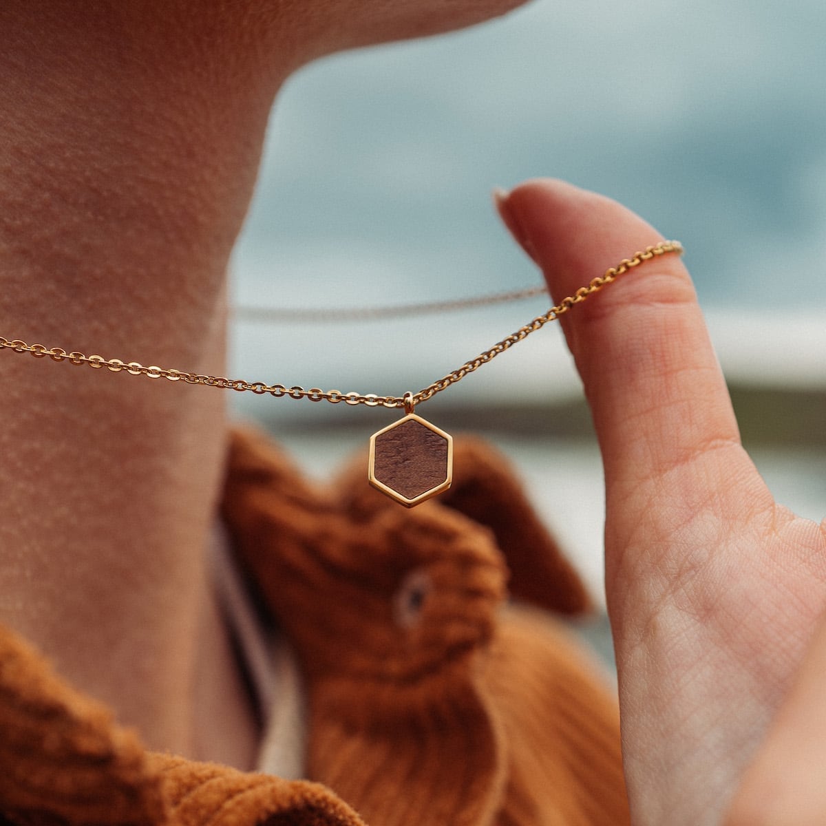 "Facade Necklace" necklace in walnut and gold with a hexagonal pendant, showcasing a modern and elegant style.