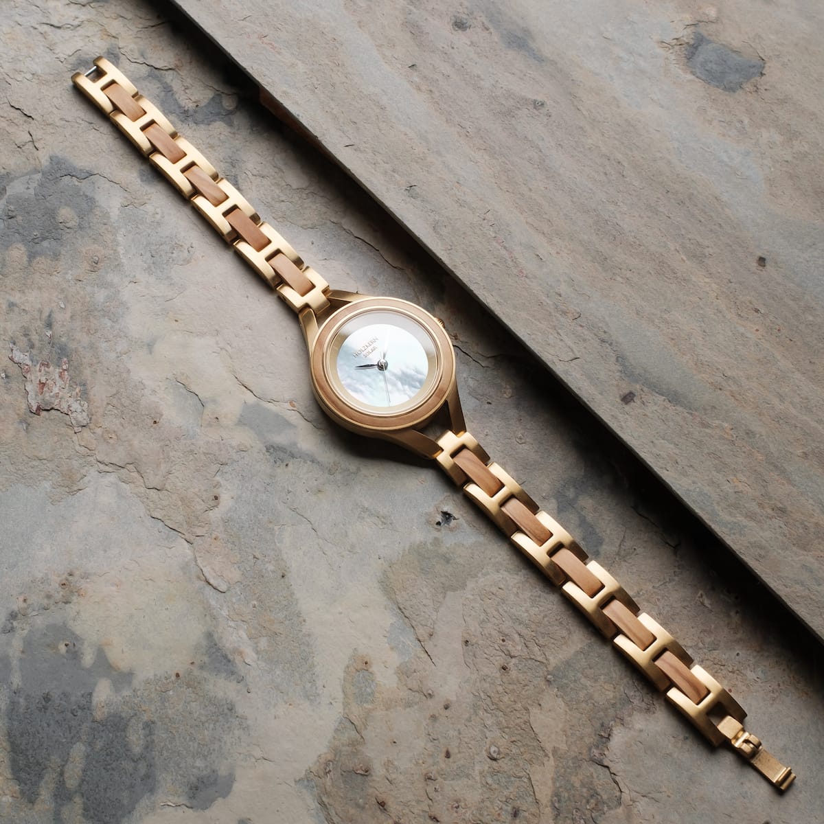 "Tumi" watch, featuring an olive and nacre design with a sleek metal band.
