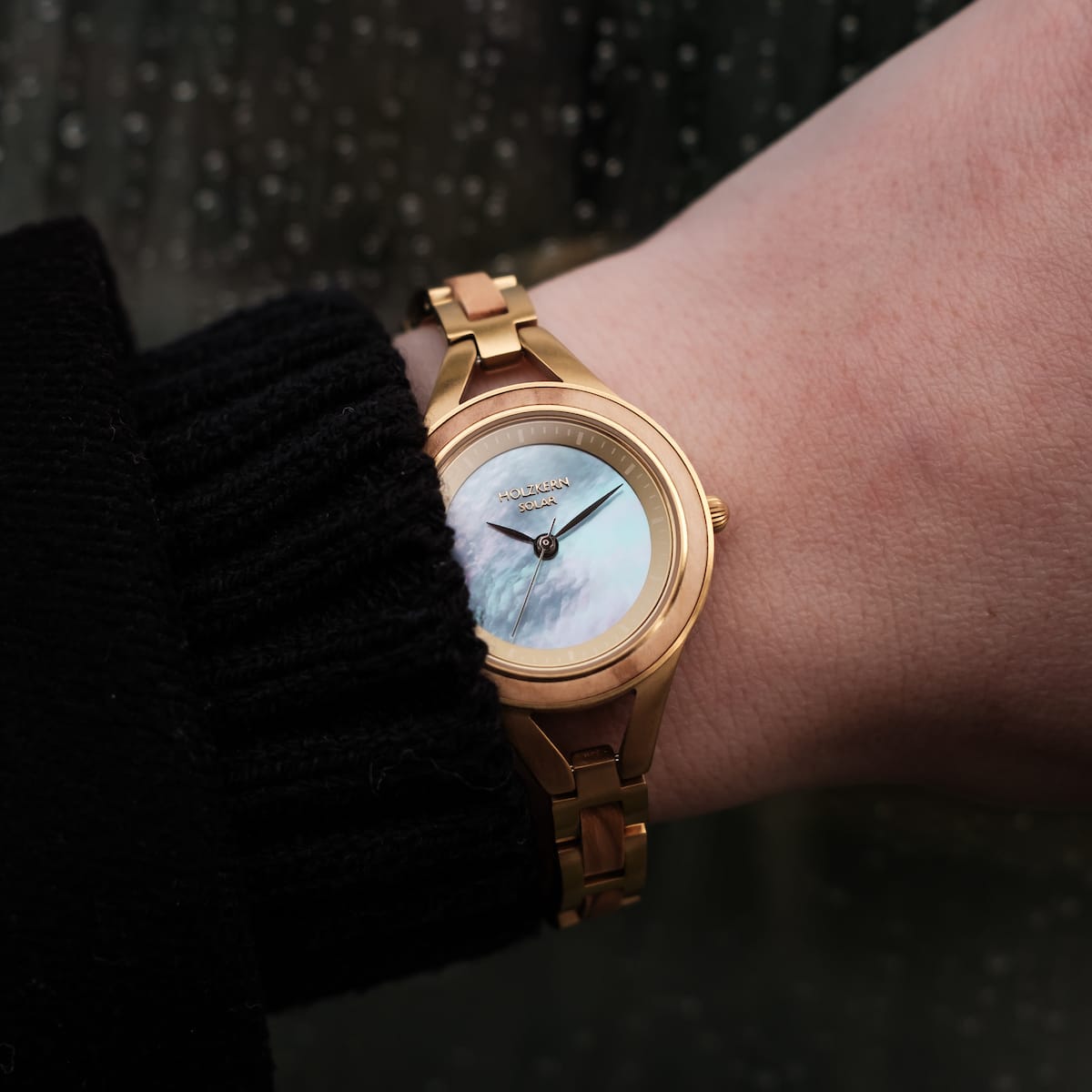 "Tumi" watch with olive accents and nacre styling on wrist, featuring a classic and elegant visual design.