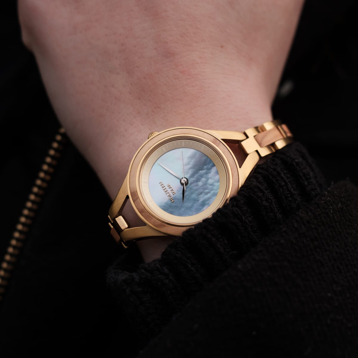 "Tumi" watch with an elegant olive case and nacre dial on a wrist.