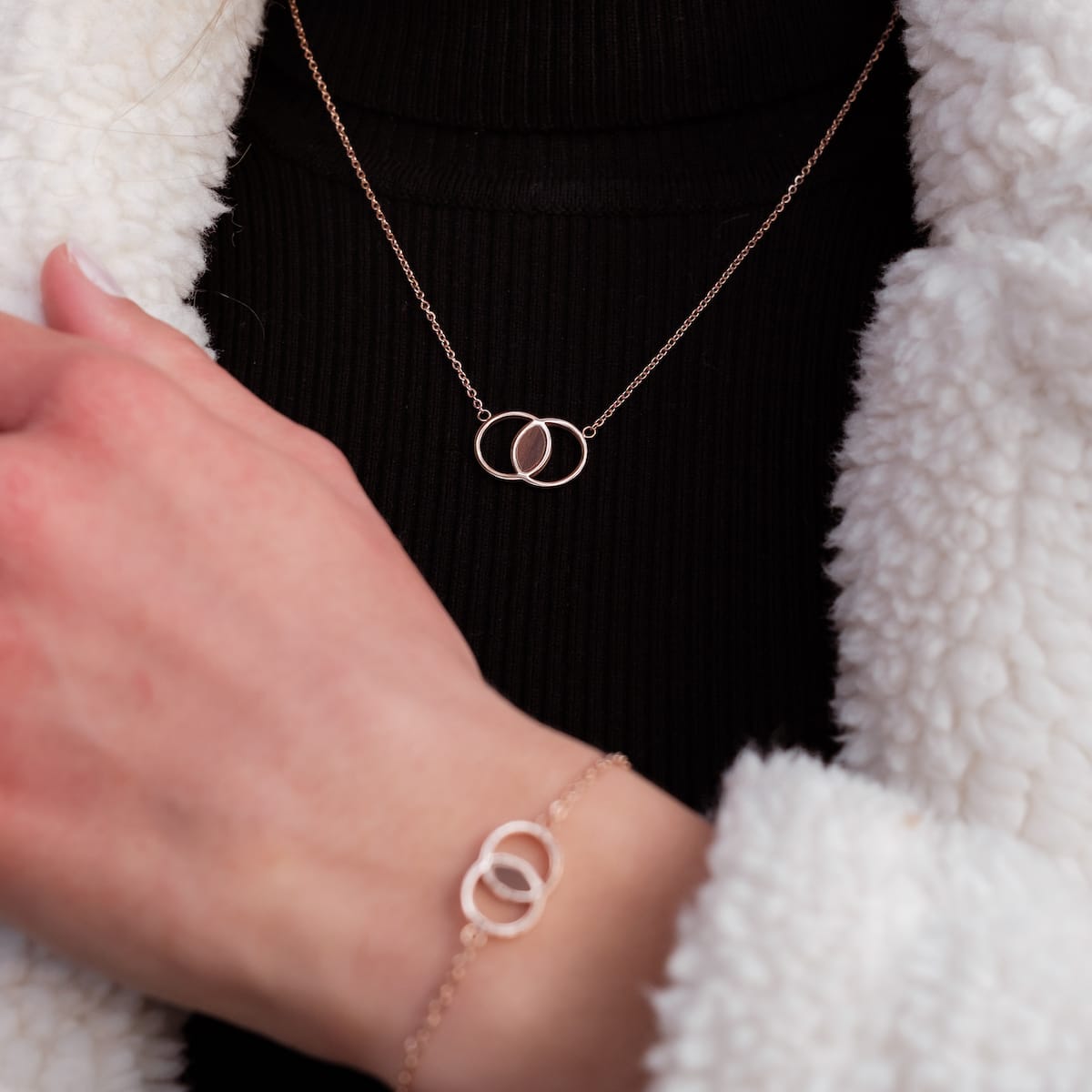 "Effigy Necklace" necklace, featuring intertwined walnut and rose gold rings, elegantly worn by a person in a stylish setting.