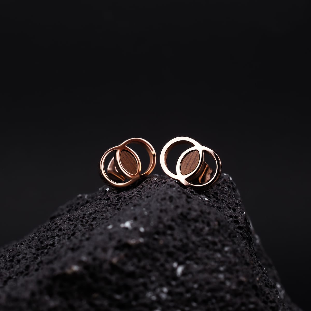 Effigy earrings in Walnut and Rose gold with a modern, circular design on a dark textured background.