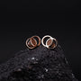 Effigy earrings in Walnut and Rose gold with a modern, circular design on a dark textured background.