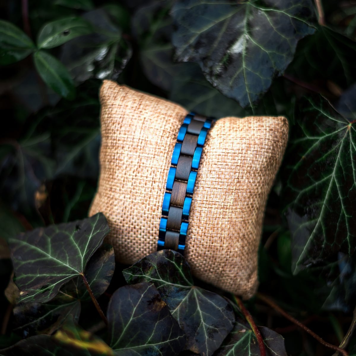 "Triad" bracelet, featuring a maple and blue design, styled elegantly on a rustic cushion surrounded by foliage.