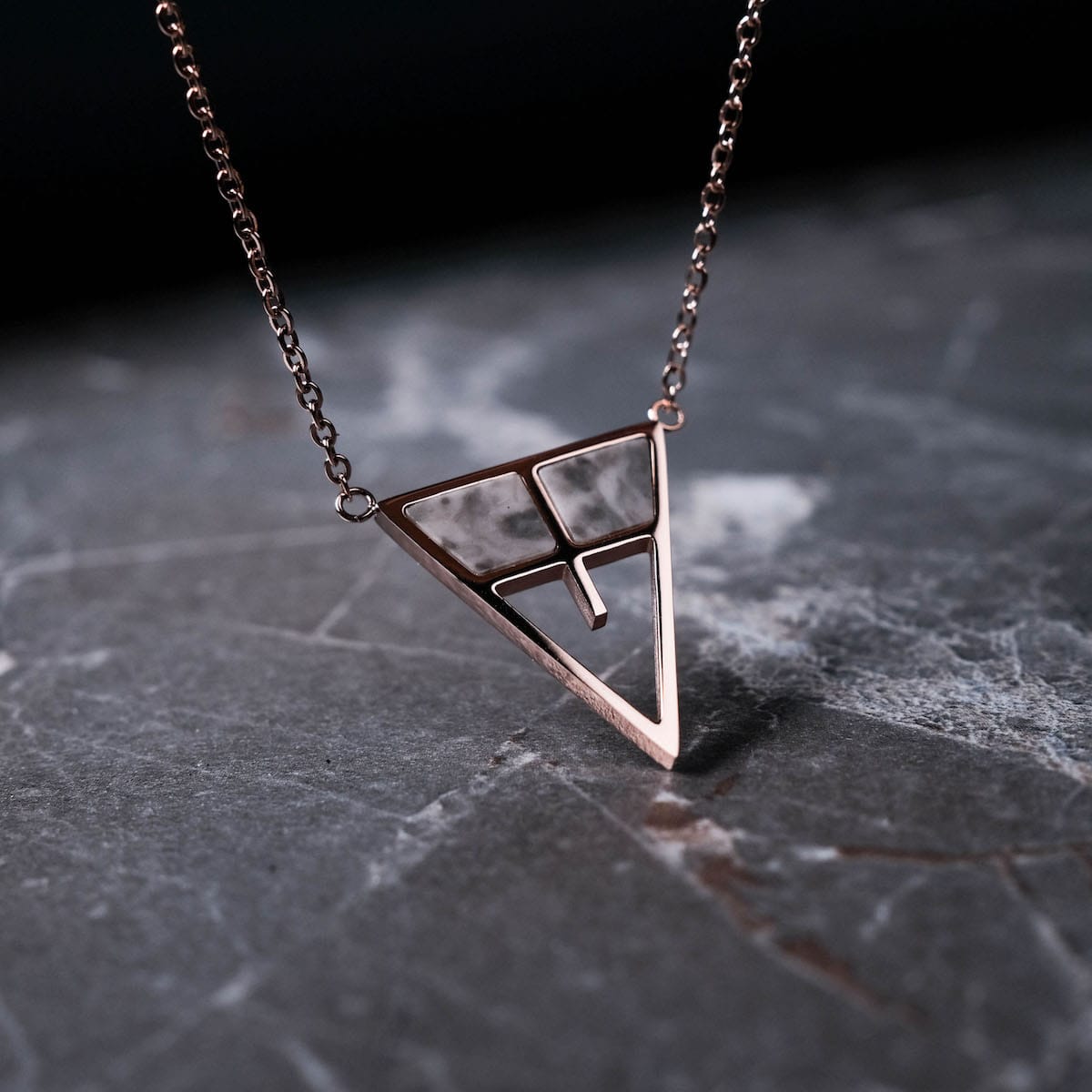 "Chiaroscuro Necklace: A geometric necklace in gray marble and rose gold, featuring a striking triangular design."