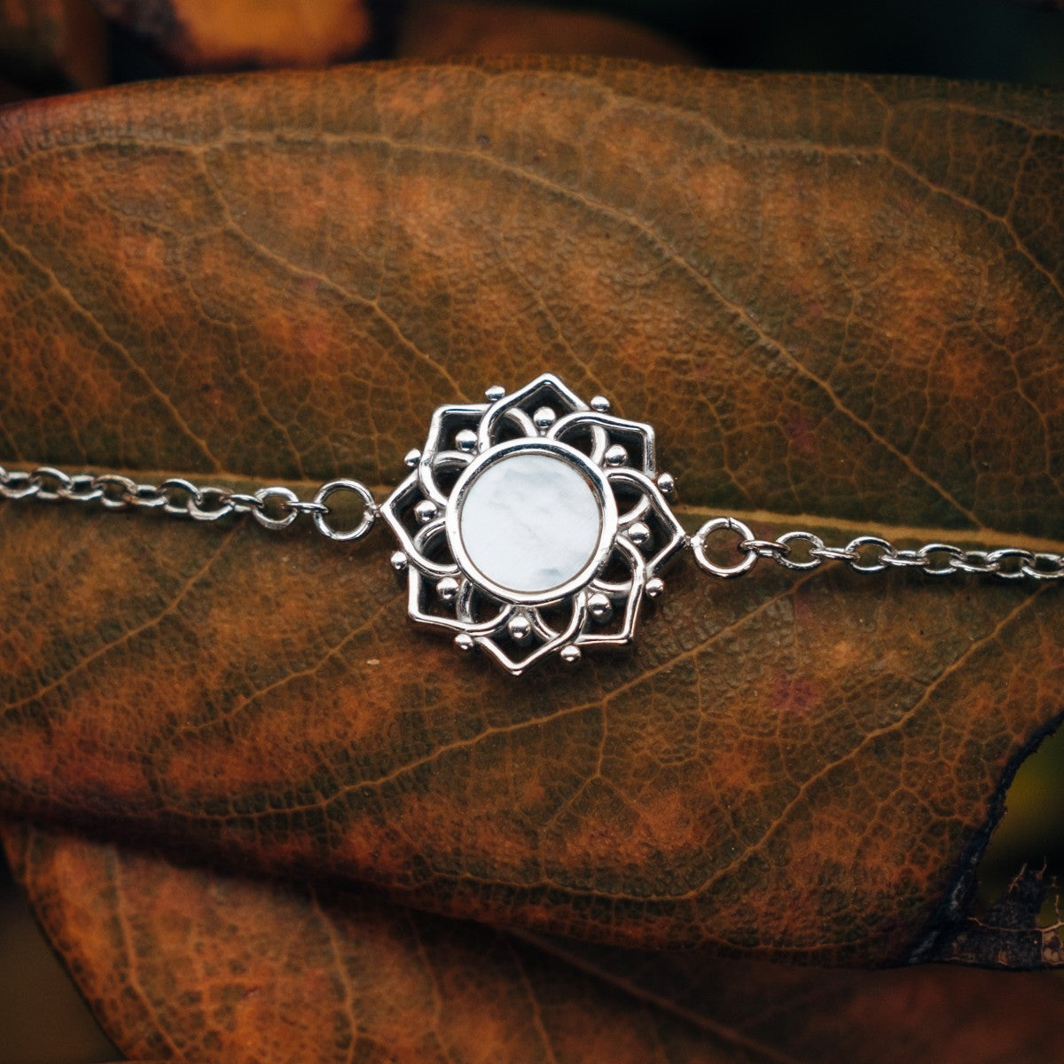 "Composition Bracelet", a delicate bracelet featuring white nacre and silver with intricate design on a textured leaf background.