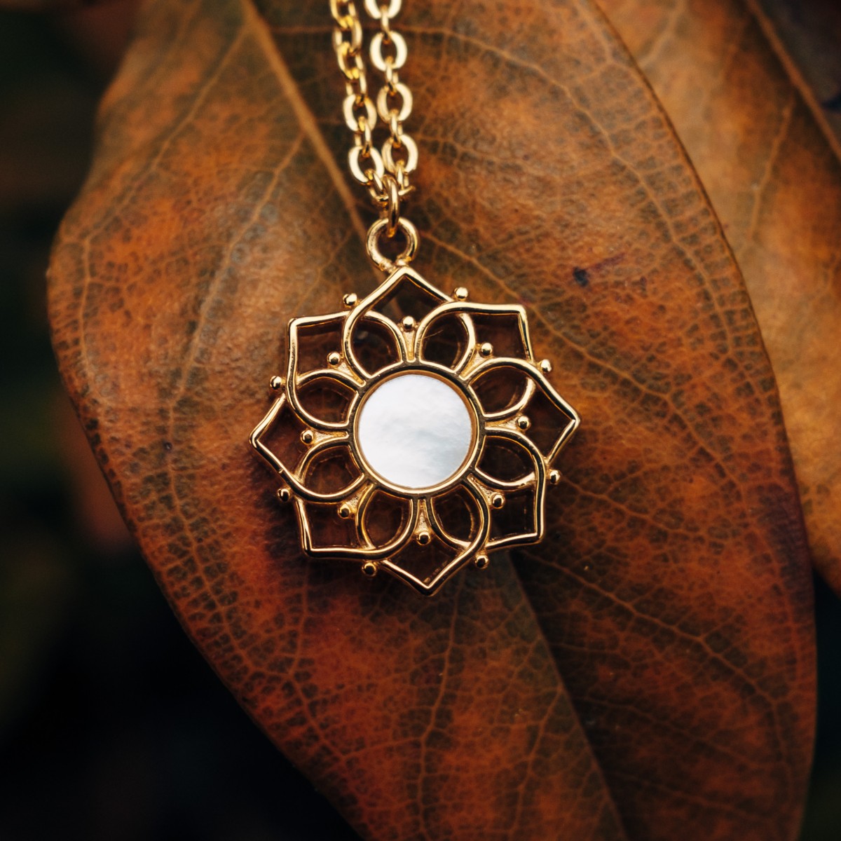 "Composition Necklace" necklace in gold with white nacre, featuring an intricate floral design on a leaf background.