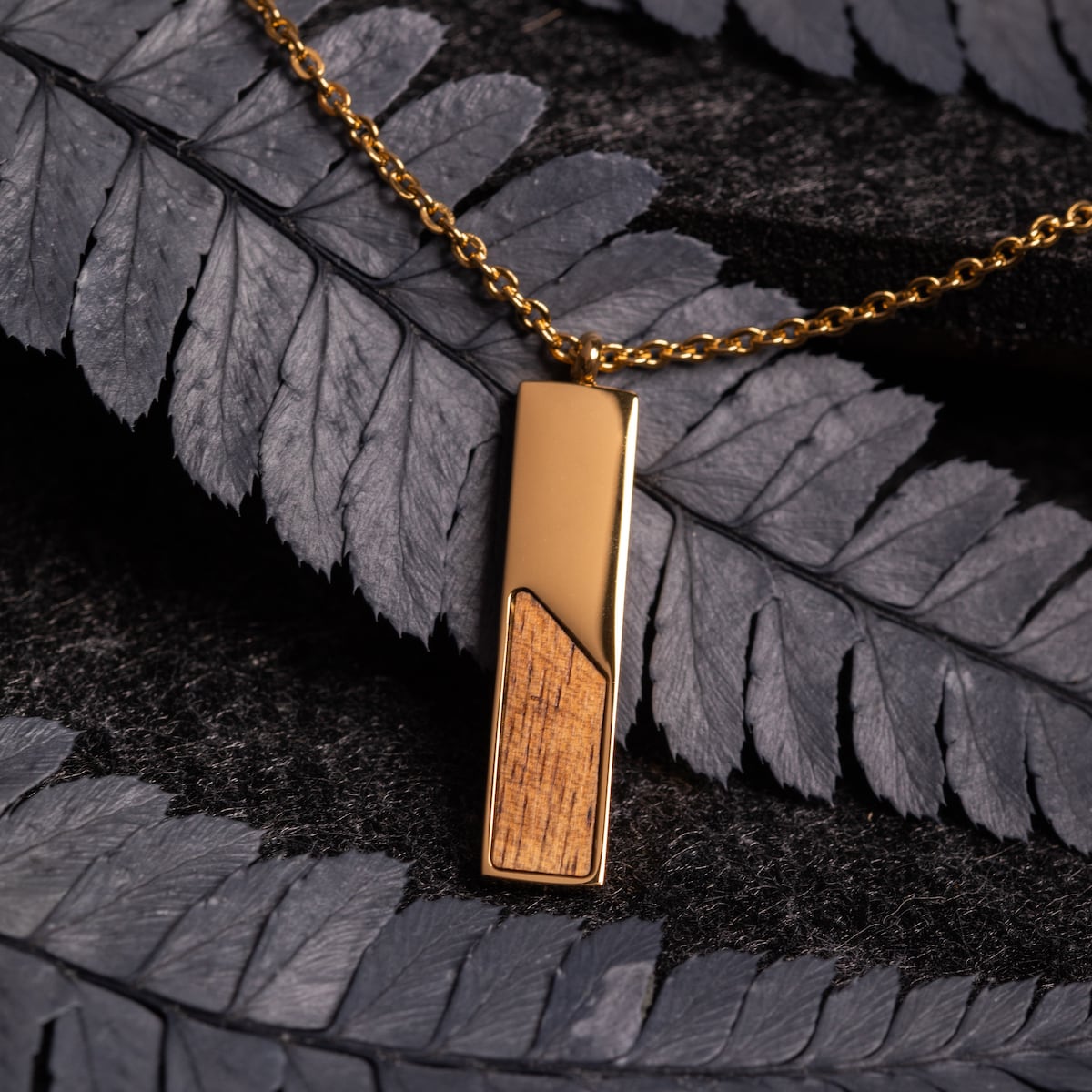 "Ephemera Necklace" sleek necklace featuring Koa wood and gold accents against a textured background.