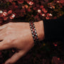 "Triad" bracelet featuring a stylish amaranth and gray design on a wrist amidst autumn foliage.
