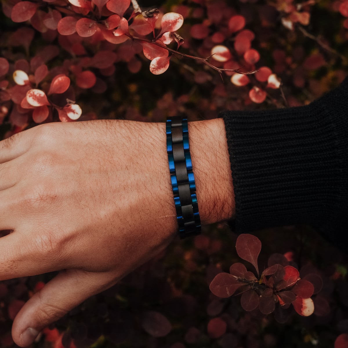 "Triad" bracelet with a maple and blue design, worn against a backdrop of red foliage.