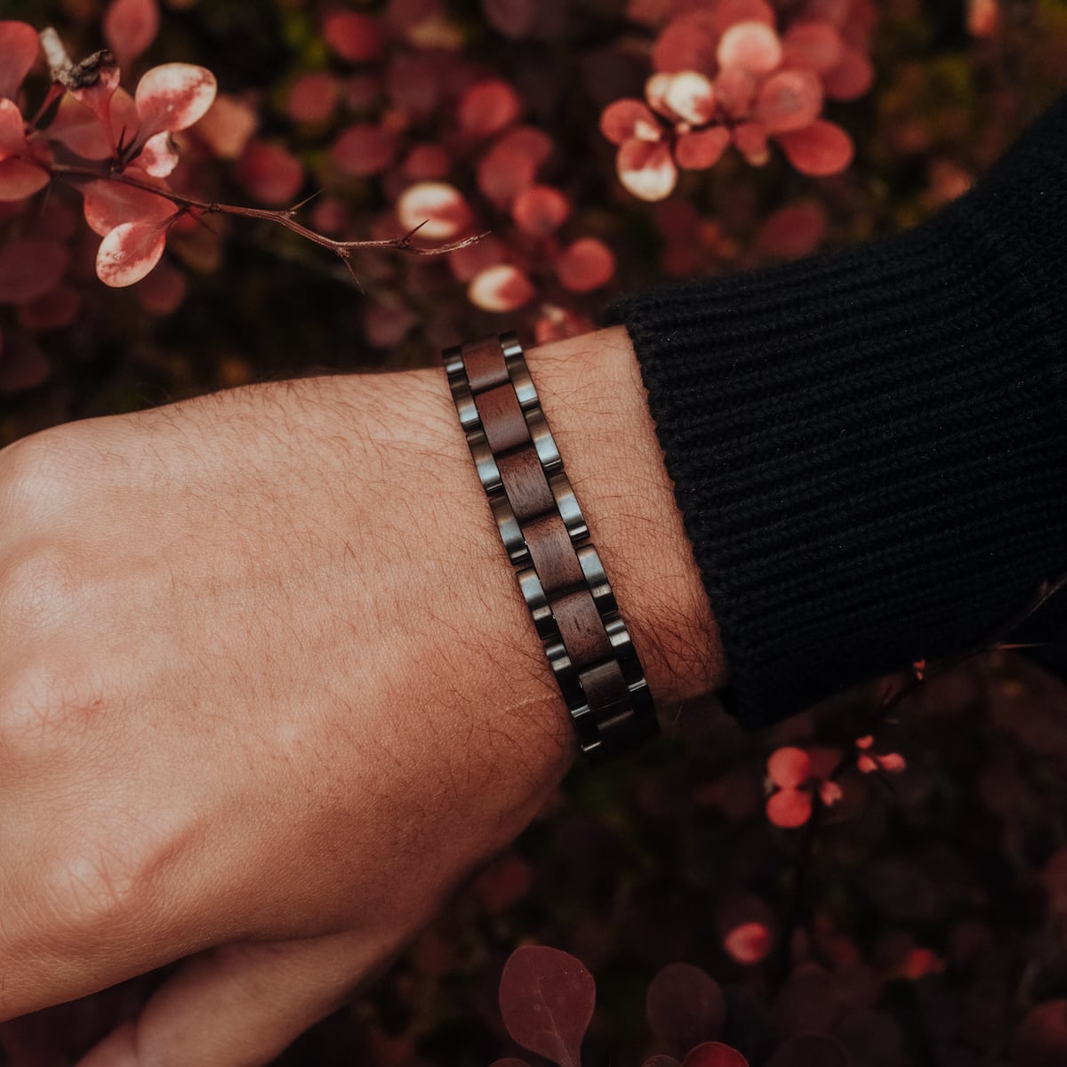 "Triad" bracelet, featuring a sleek walnut and gray design, on a wrist amidst vibrant foliage.