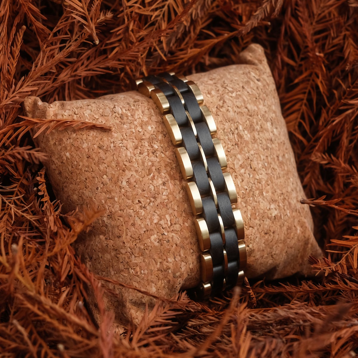 "Kanon" wristband, featuring a black maple and gold design, presented on a cork cushion amidst autumn leaves.