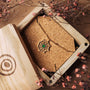 "Aphonia Necklace", an elegant gold necklace featuring a green marble pendant, displayed in an ornate wooden box with floral accents.