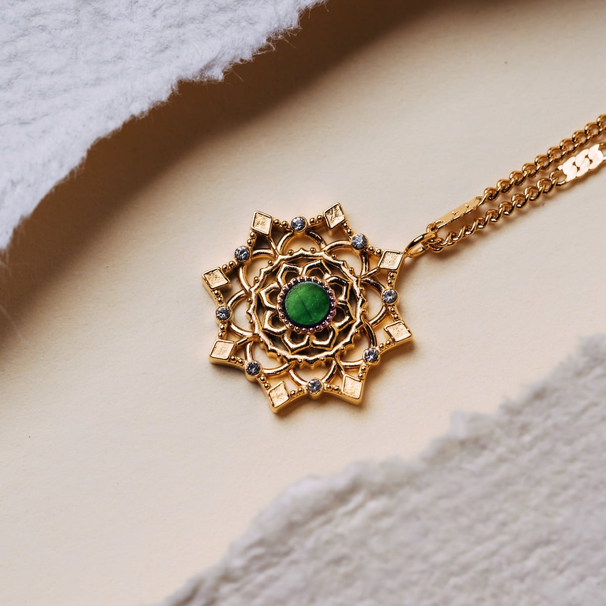 "Aphonia Necklace" necklace with a green marble centerpiece set in gold, featuring an intricate design pattern.