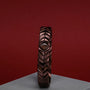 "Prelude" bracelet with a walnut and copper design, featuring a geometric style against a red background.