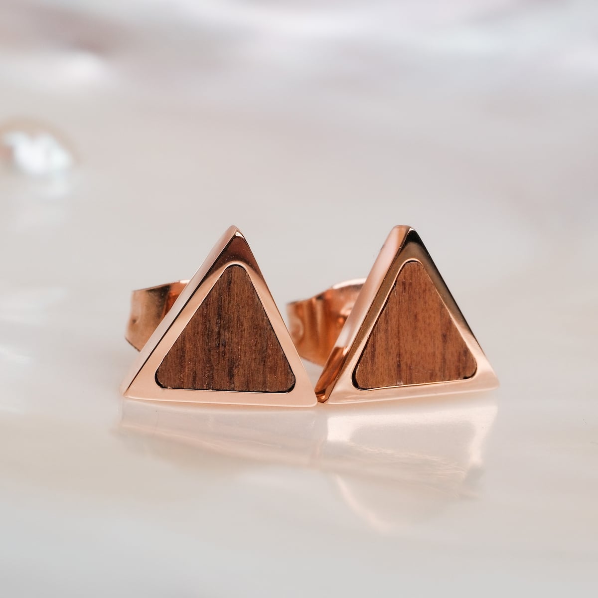 "Scale Earrings" are triangle earrings featuring walnut wood and rose gold accents, offering a sleek, modern style.