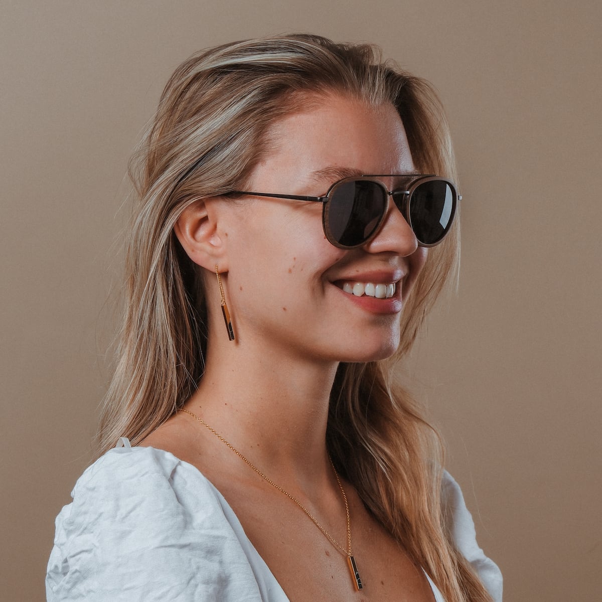 "The Risky" sunglasses in walnut and dark gray, featuring a sleek and modern style worn by a smiling individual.