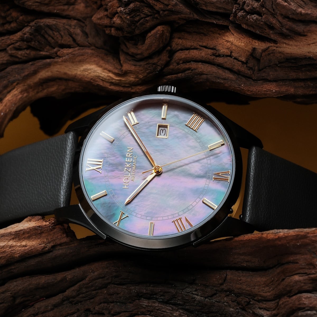 "Milestones" wristwatch featuring a nacre dial and dark gray strap, elegantly styled on wood background.