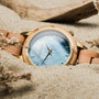 "Antrim" watch featuring an olive-toned wooden band and a nacre style face in a sandy beach setting.