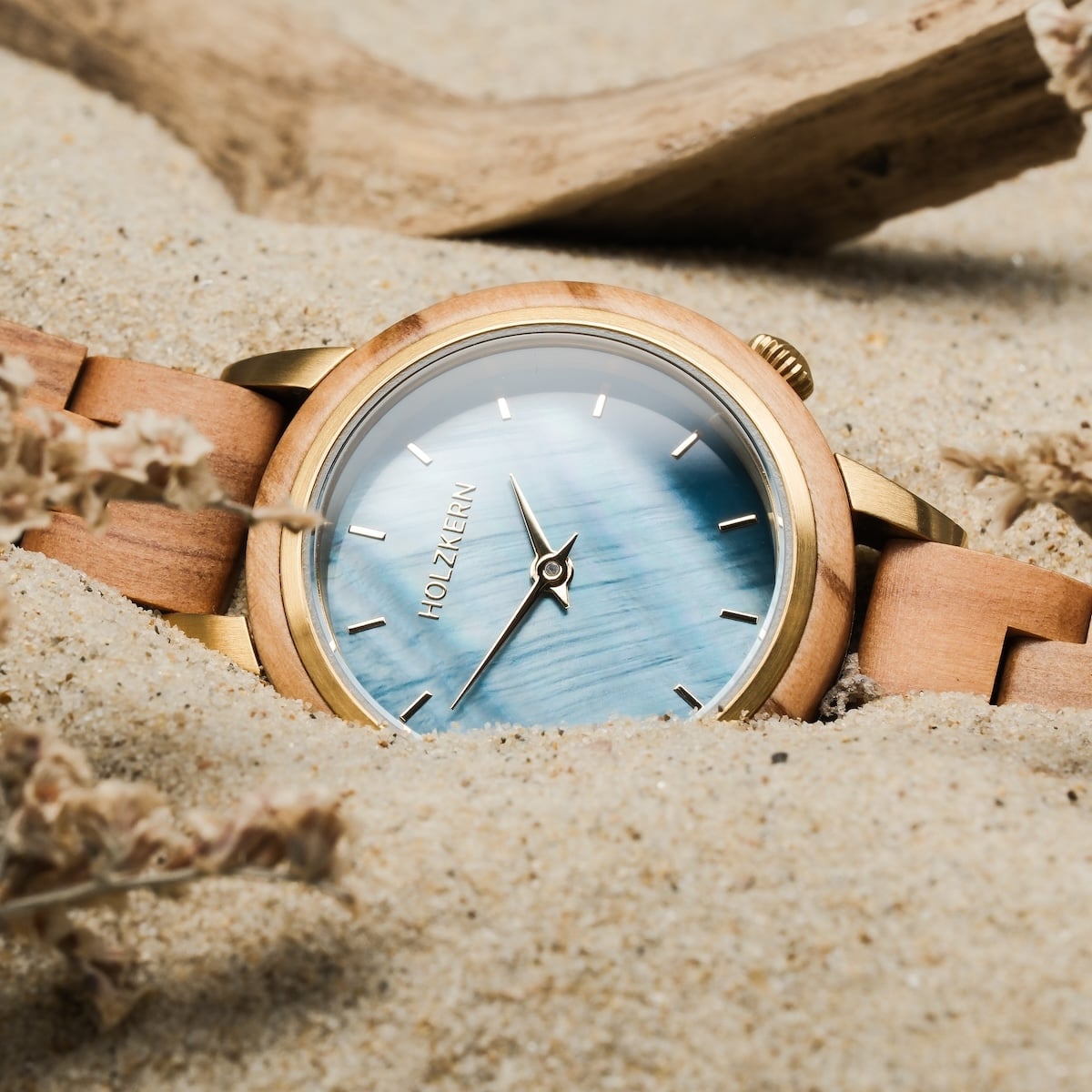 "Antrim" watch featuring an olive-toned wooden band and a nacre style face in a sandy beach setting.