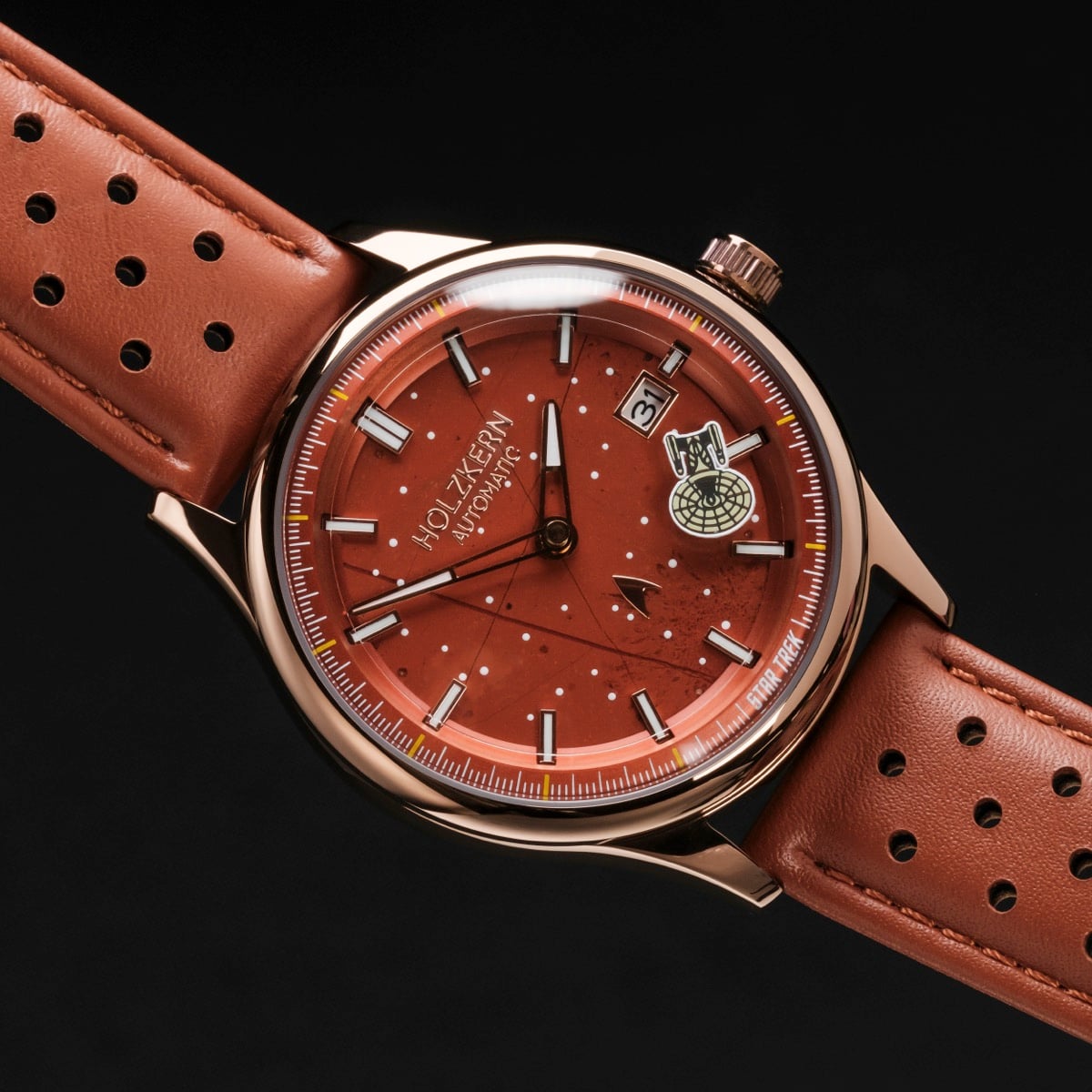 "NCC-1701-D" watch with a jasper red face, rose gold accents, and a brown perforated leather strap.