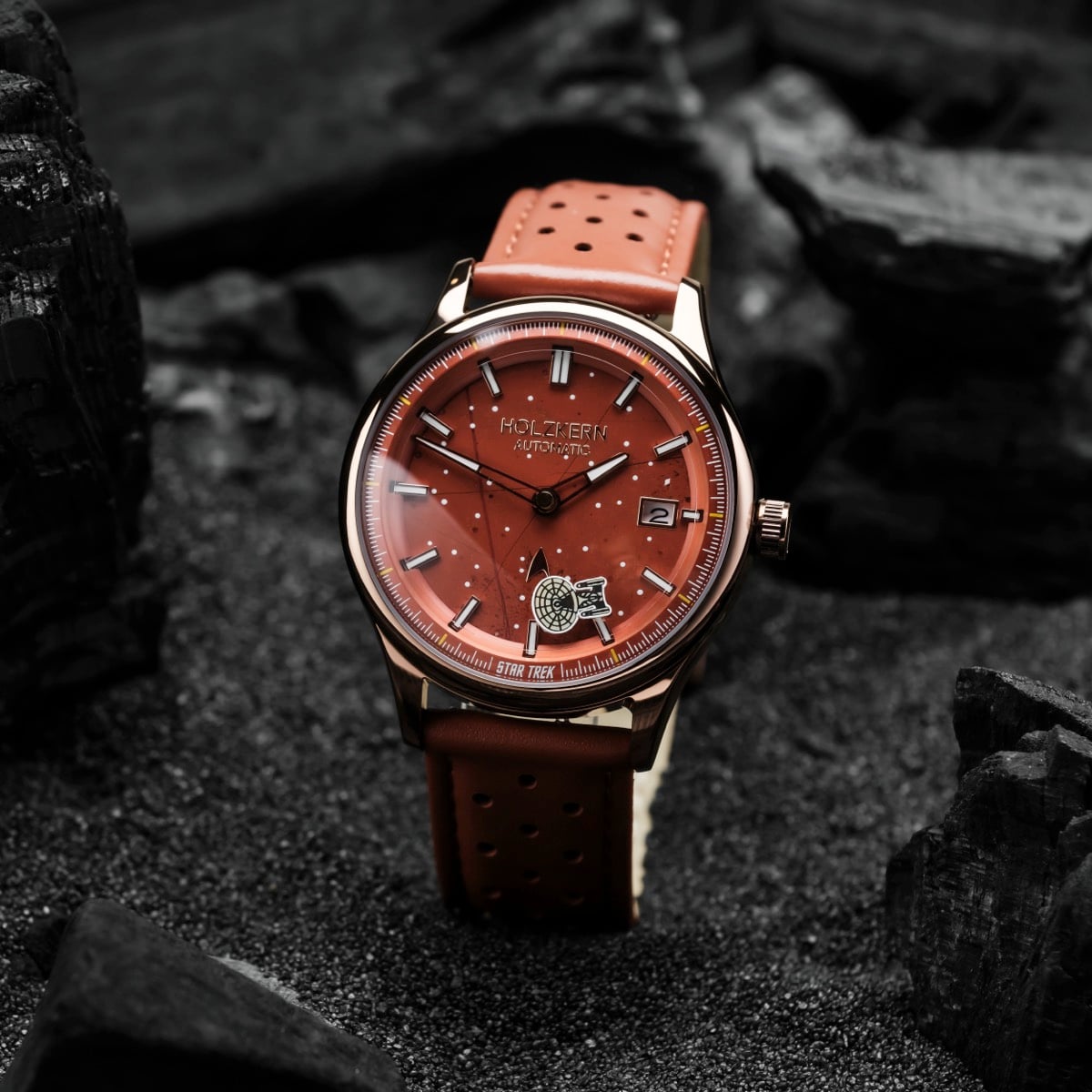 "NCC-1701-D" watch with red dial and strap, featuring sleek, modern design on a textured dark background.