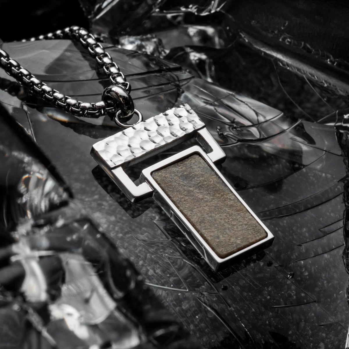 "Transcendent" necklace featuring a hammered silver design with a slate insert on a reflective surface.